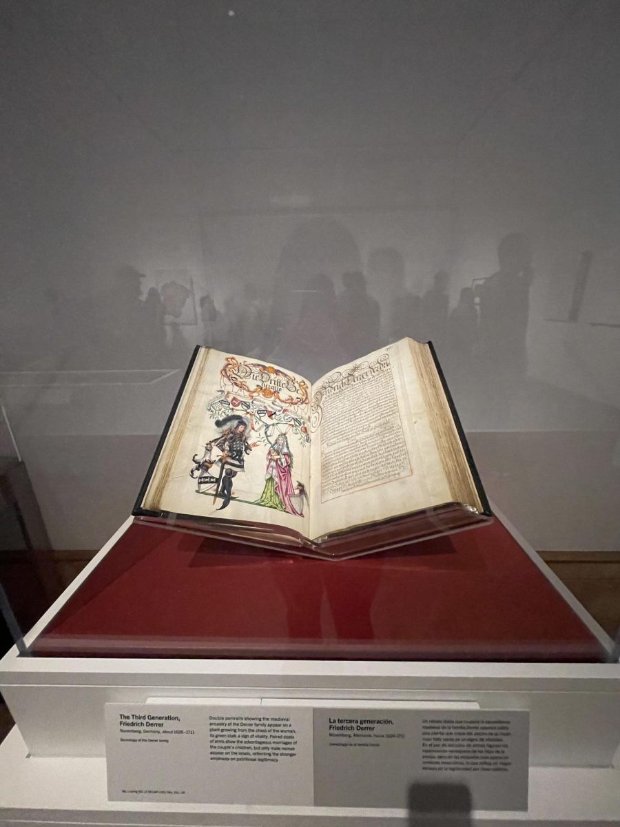 A case with an ancient book reflecting the other people roaming in the exhibit. The book was made during a time were this style of art flourished, this specific piece of art representing the medieval ancestry of the Derrer family.